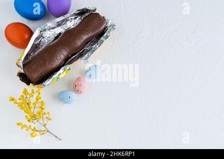 Easter eggs and chocolate bunny on white background with yellow flower decorations. Top view. Copy space. Stock Photo