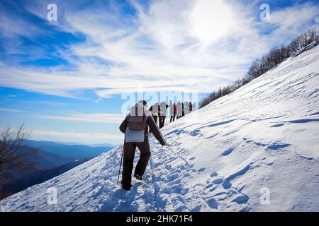 Group of mountain hikers in single file go up the snowy peak. In the background the cloudy blue sky. Stock Photo