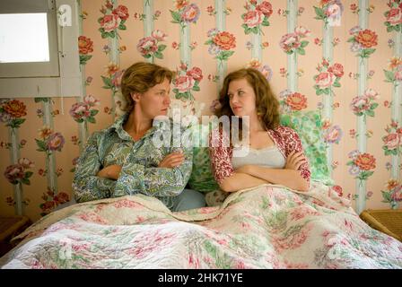 Young couple laying in bed looking sideways at each other in bedroom with floral wallpaper walls Stock Photo