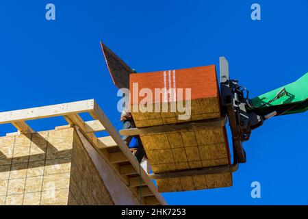 Residential house under construction worker is covering the wooden frame with plywood using hydraulic hammer making ridge on the roof Stock Photo