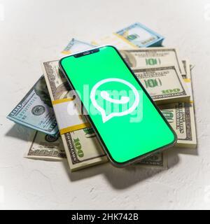 Berlin, Germany - February 02, 2022: Apple iPhone 12 Pro with messenger WhatsApp on the screen and dollar money Stock Photo