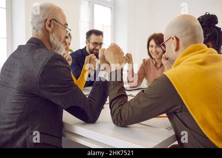 Team of happy business colleagues sitting together around table, holding hands and smiling Stock Photo