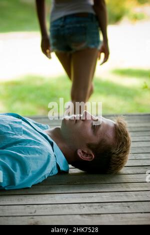 Young man laying down on porch with woman standing in back Stock Photo