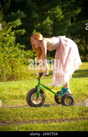 Young redheaded woman riding a child's tricycle Stock Photo