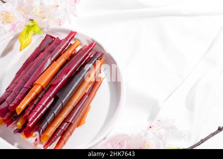 Colorful fruit leather rolls on a plate on light background Stock Photo