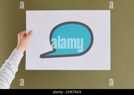White paper with drawn blue chat message icons in hand of unknown woman on green background. Stock Photo