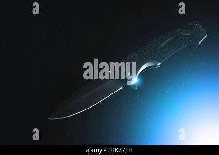 Tactical folding knife on dark background is illuminated by bright blue light Stock Photo