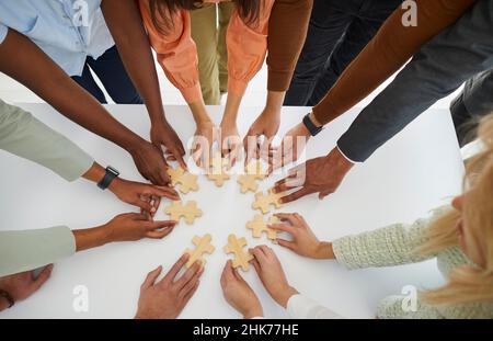 Hands of different business people connecting puzzle pieces as sign of problem solving and teamwork. Stock Photo