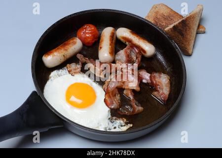 Fried egg, fried bacon and sausages in pan Stock Photo