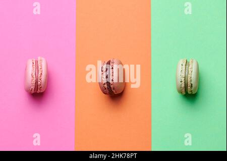 three colored macarons in pink, brown and green on matching colored background Stock Photo