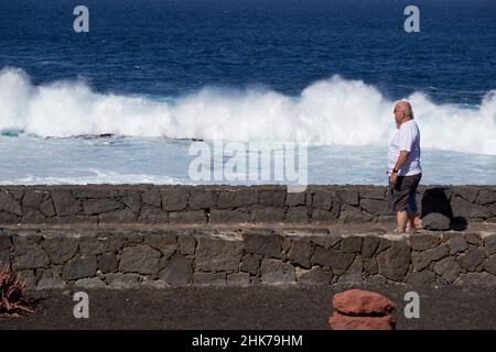 elderly couple on teh espanade watching atlantic waves breaking near western shoreline of Punta Pechiguera playa blanca Lanzarote Canary Islands Spain Stock Photo