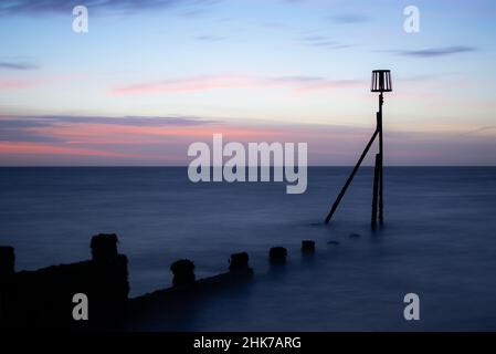 A beautiful sunrise on Dovercourt Beach in North Essex, UK.  A wooden breakwater leads in to the North Sea and is finished with a metal marker beacon Stock Photo