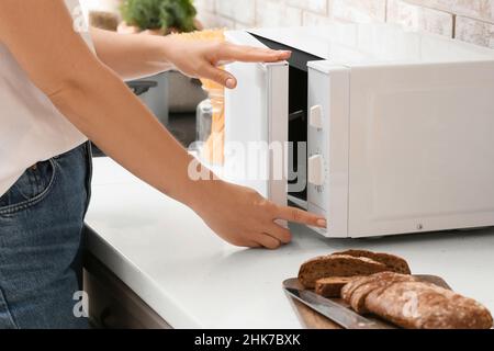 Woman opening microwave oven in kitchen Stock Photo