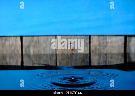 Circles and splash on water from raindrops on background an old fence and blue sky Stock Photo