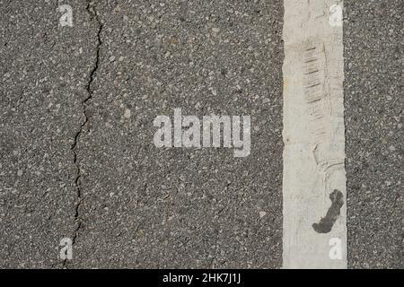 Crack in asphalt parallell white painted line with tire marks and feature. Stock Photo