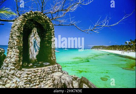 The Christian Shrine on Willy's Rock at White Beach on Boracay Island in the Western Visayas region of the Philippines. The oddly shaped volcanic formation is topped by a statue of the Virgin Mary. It is surrounded by the shallow, pastel blue-green waters of the Sulu Sea along the shores of the 4-kilometre White Beach.