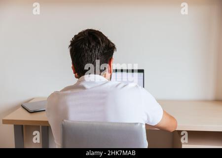 Young man on his back in a white polo shirt working at home or watching a class in his room. Concept: teleworking or having online classes. Stock Photo