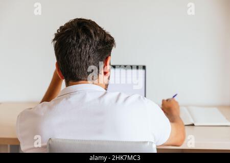 Young man on his back in a white polo shirt working at home or watching a class in his room. Concept: teleworking or having online classes. Stock Photo