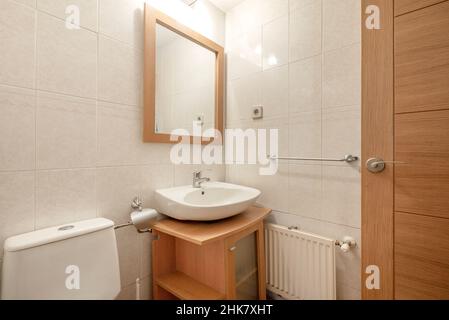 Modern bathroom with light wood cabinet and square mirror with wood frame and white china sink Stock Photo