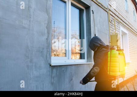 Coronavirus disinfection. People in hood making disinfection in house outdoor, copy space, hot steam disinfection. Male worker spraying insecticide on Stock Photo