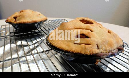 Two homemade apple pies in mini pie pans on a cooling rack over tin foil; home cooking and baking. Stock Photo