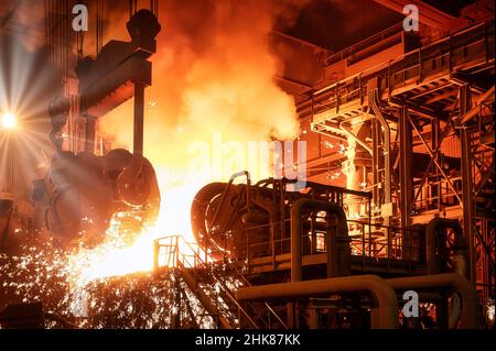 The molten metal is poured from the ladle into the metallurgical furnace. Stock Photo