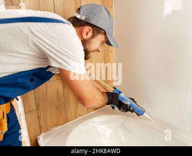 Concentrated plumber caulking bath tube with silicone glue using cartridge in bathroom Stock Photo