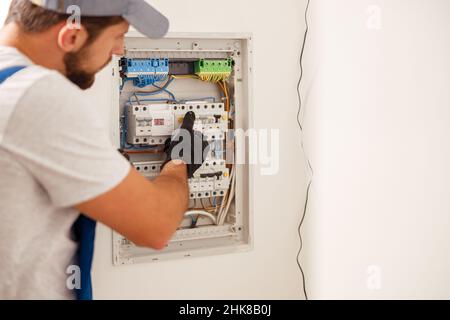 Electrical technician in uniform looking focused while working in a switchboard with fuses Stock Photo