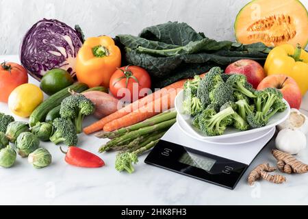 A dish full of broccoli on a food scale with a variety of produce in behind. Stock Photo