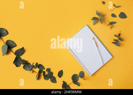 Eucalyptus leaves and a notebook with a pencil on a yellow background. Top view. Flat lay. Place for text, copy space. Stock Photo
