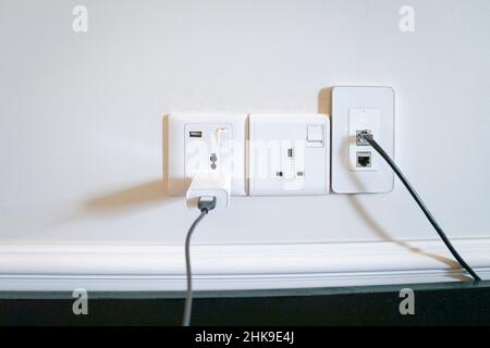 Electric power outlets on the wall with data and charging cable connected. Stock Photo