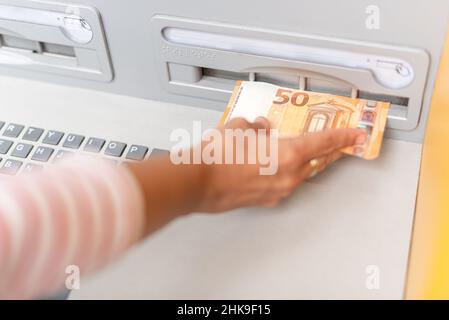 Crop woman putting money on card in ATM Stock Photo