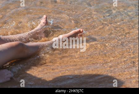 Close up child's legs relaxing in sea water on the beach, sunny day light in a morning, blank space for text and design.
