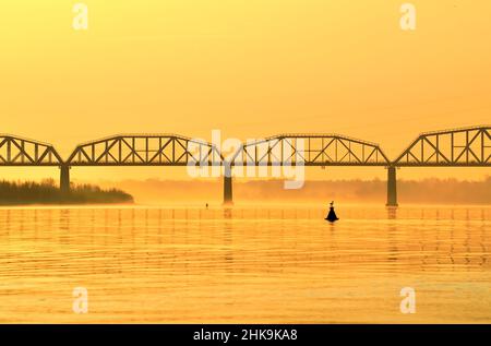The bank of the Ob River. Railway bridge in the morning fog in the morning golden light Novosibirsk, Siberia, Russia, 2021 Stock Photo