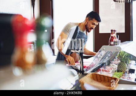 Young man butcher arranging meat products in display case of butcher shop Stock Photo