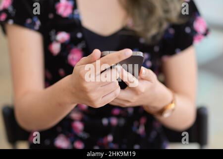 Close-up image of a female in casual outfit sitting on armchair and using her mobile phone. Stock Photo