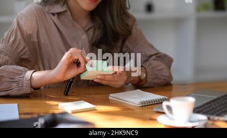 Asian female marketing officer taking her creative ideas on memo pad sticky notes at her office desk. Stock Photo