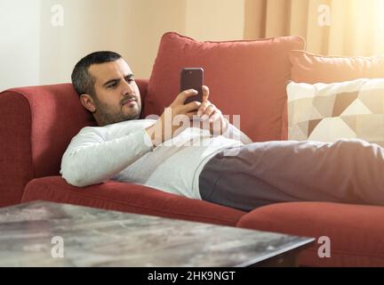Close up photo of man using smartphone while relaxing on comfortable sofa. Modern house concept. Stock Photo