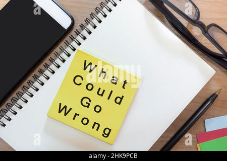 Text on yellow note with notepad on wooden desk - What could go wrong. Business and audit concept Stock Photo