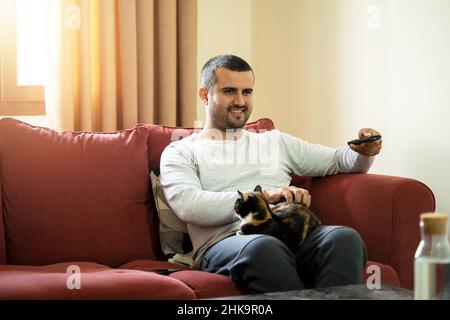 Close up photo of man holding tv remote control and relaxing with the cat. concept of tv watching. Stock Photo