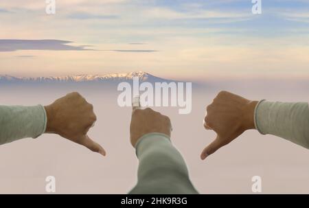One hand pointing up, others pointing down on mountain peak background. Concept of faith, motivation, foresight, goal. Stock Photo