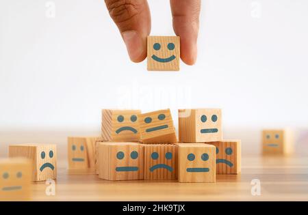 Hand picking smiling face wooden cube. Symbol of costumer service review. Concept of advantages and benefits of smiling face in business. Stock Photo