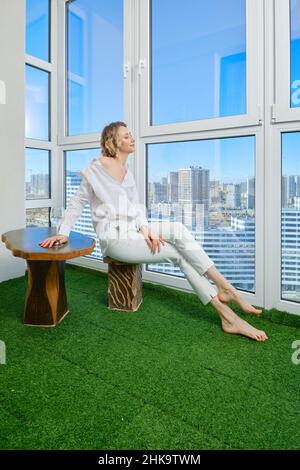 Barefoot woman sits on the balcony of her new apartment and admires the view of the city from the window Stock Photo