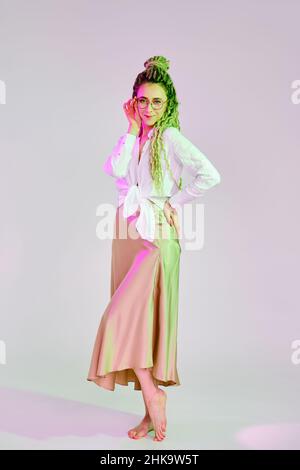 Full length portrait of a woman in linen shirt and silk skirt touching the bow of glasses Stock Photo