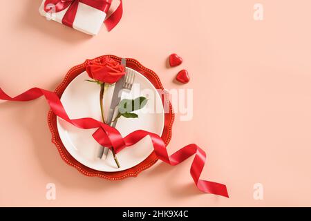 Valentines day table place setting with gift, roses, hearts on pink background. View from above. Valentine's greeting card. Invitation to dinner. Stock Photo