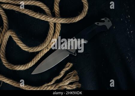 Tactical folding knife for survival, active lifestyle and recreation, on rope background and dark background Stock Photo