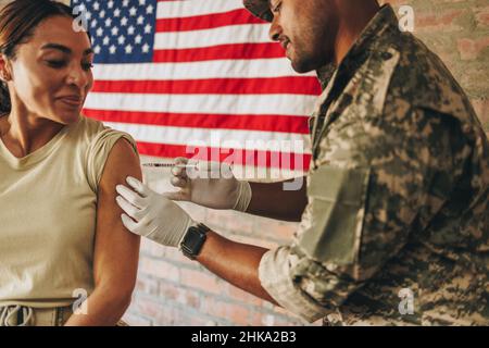 Young military physician vaccinating a female soldier against coronavirus disease. American military doctor injecting a female soldier with the covid- Stock Photo