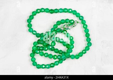 tangled handcrafted necklace from emerald green tinted agate beads on gray concrete board Stock Photo