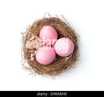 Three pink eggs in a nest decorated with flowers on a white background. Top view, close-up. The concept of Easter. Stock Photo