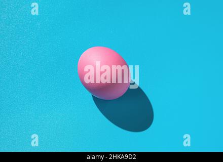 Pink egg on a blue background with a hard shadow. Abstract Easter background. Stock Photo